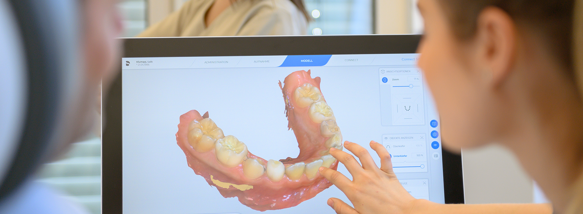 Eine Hand zeigt auf einen Monitor mit 3D Modell vom Gebiss eines Patienten