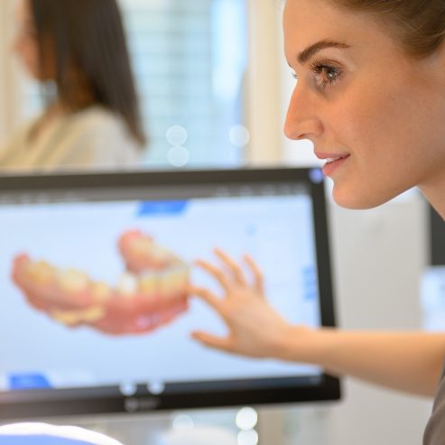 Ärztin zeigt auf einen Monitor mit 3D Modell vom Gebiss eines Patienten